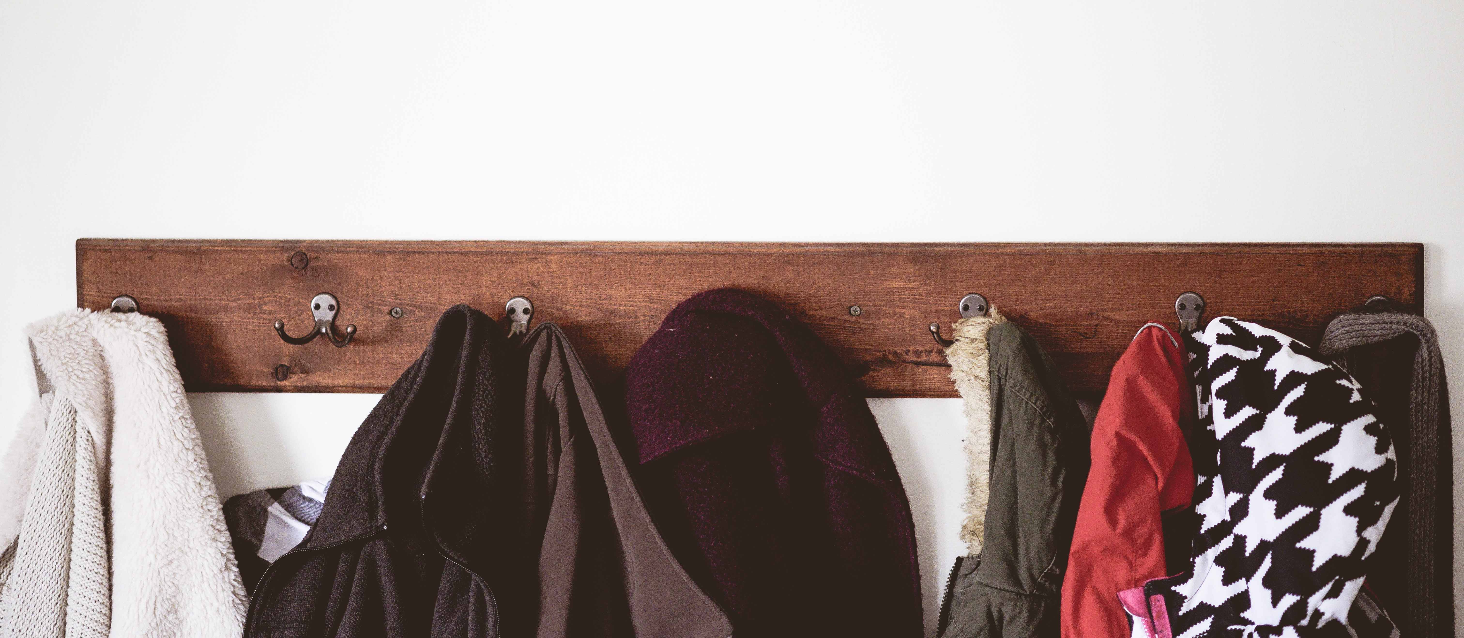 wooden coat hanger full of coats on a white wall